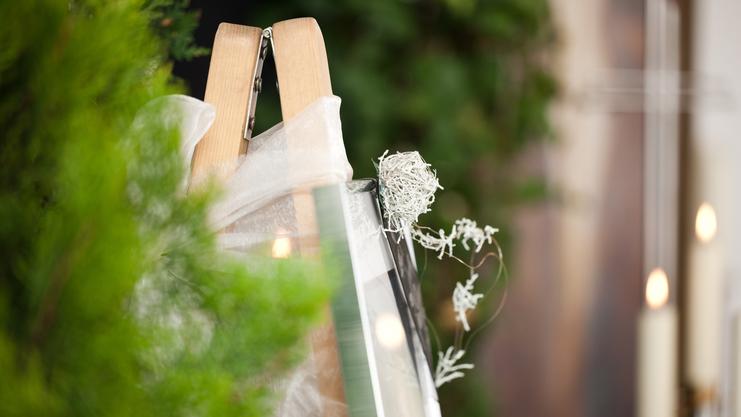 Staffelei mit einem eingewickelten Bilderrahmen und dekorativen Zweigen vor unscharfem, grünem Hintergrund.